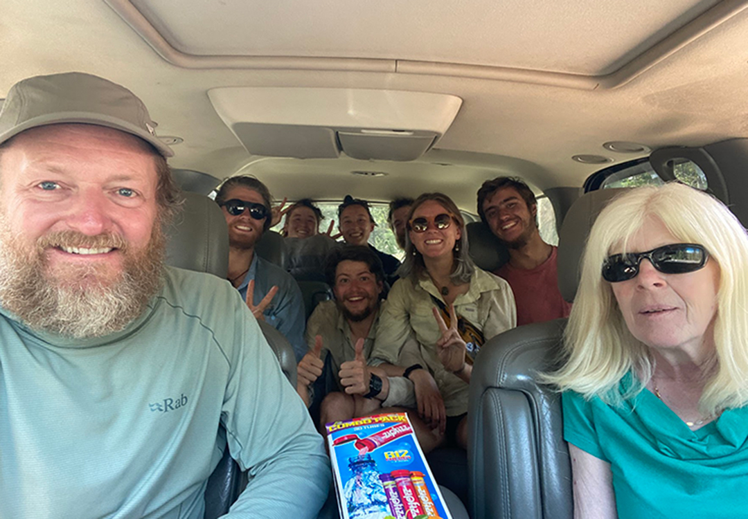 12 A group of hikers inside of a car are smiling with the driver.