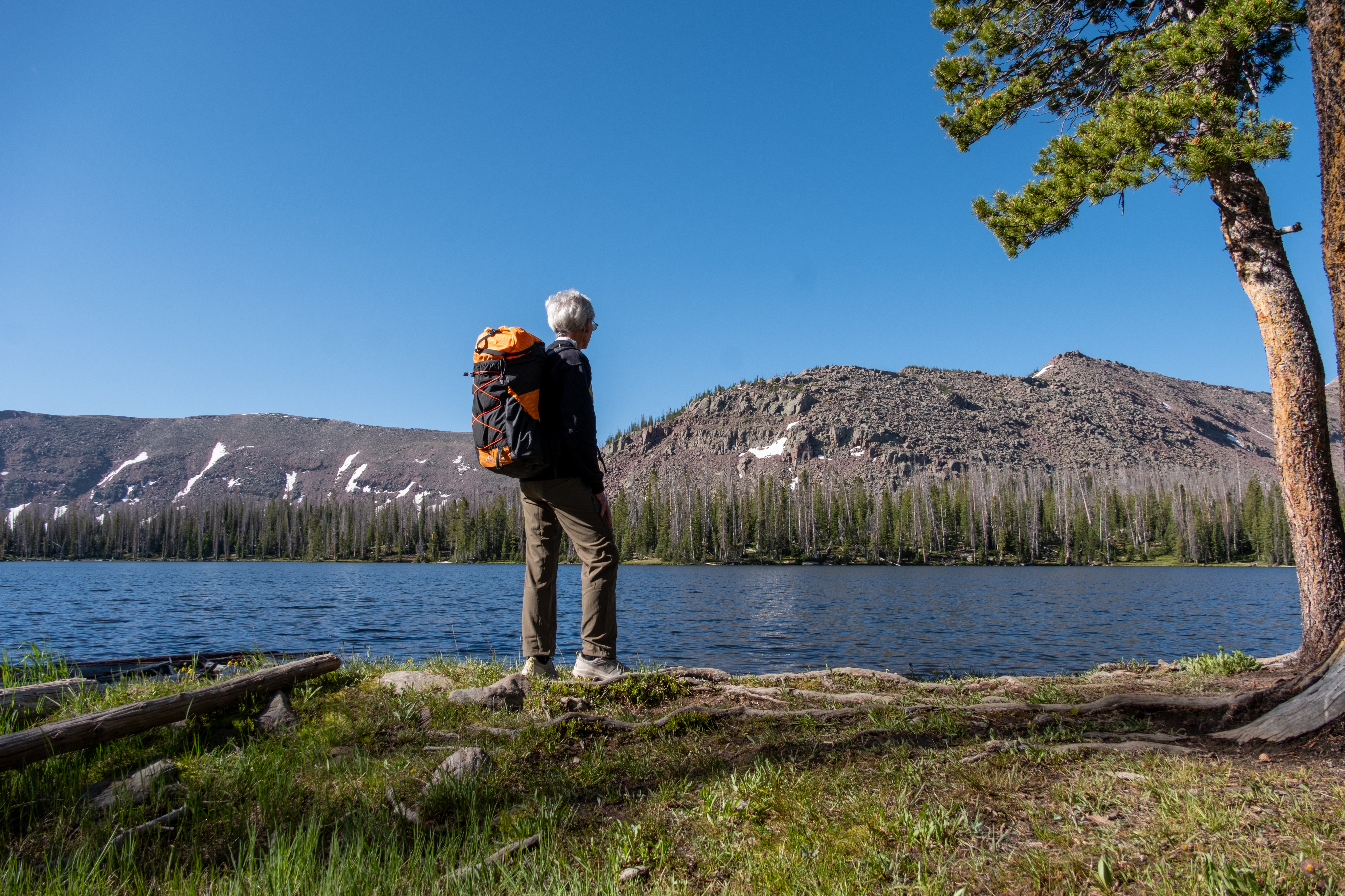 A woman poses with an orange ULA-Equipment Nexus backpack
