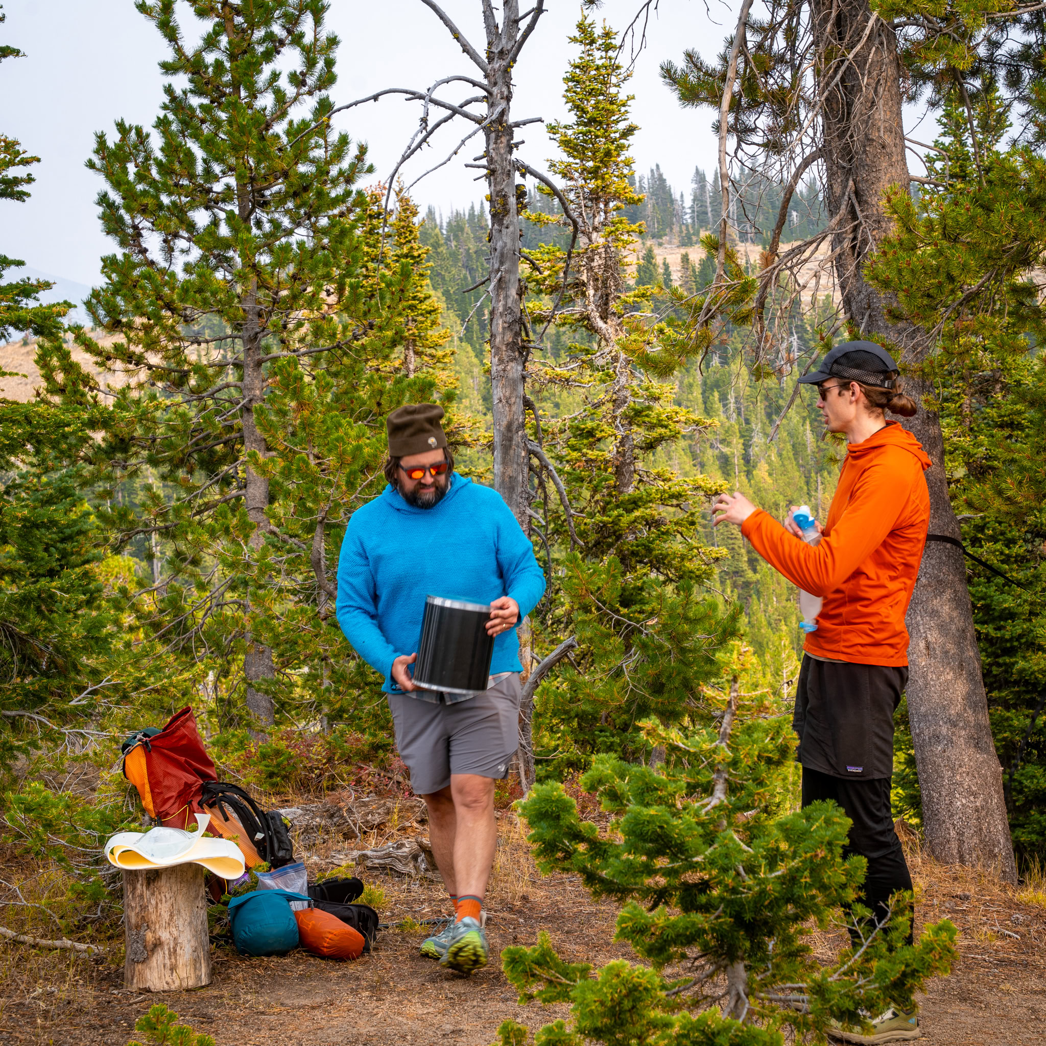 Two men on a backpacking trip handling a bear canister
